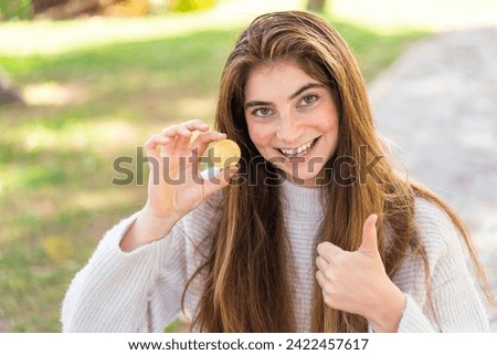 Young pretty caucasian woman holding a Bitcoin at outdoors with thumbs up because something good has happened
