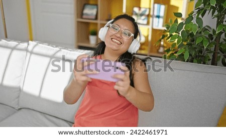 Young chinese woman watching video on smartphone sitting on sofa at home