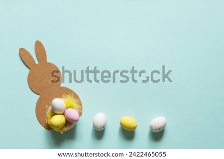 Easter concept with mockup of bunny and easter chocolate eggs, feather. Delicate pastel blue empty background with copy space. Flat lay	