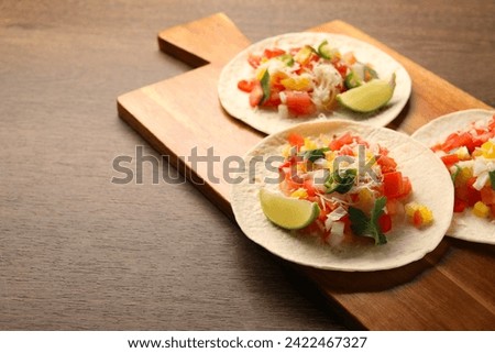 Delicious tacos with vegetables and lime on wooden table, closeup. Space for text