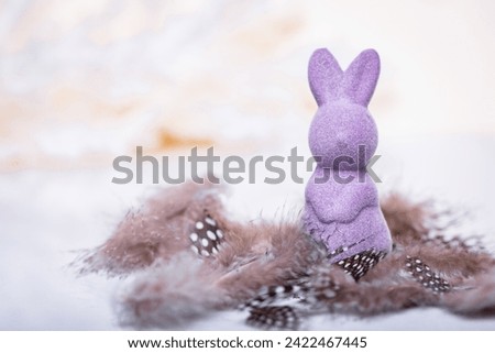 Boho-style Easter Bunny in purple amidst brown feathers on a light background. Ideal for festive décor or whimsical holiday-themed designs