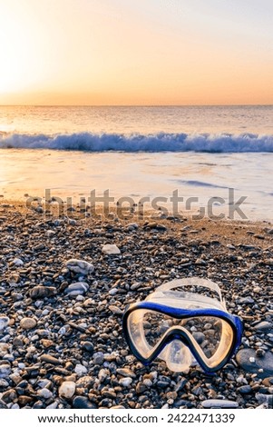 ocean cloudy morning landscape with diving mask on sea coast on foreground, sand of a beach, blue sea with surf and waves and cloudy sunset or sunrise on background