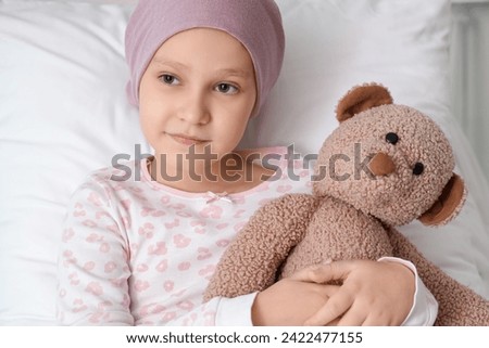 Little girl after chemotherapy with toy bear lying in bed at hospital, closeup. International Childhood Cancer Day Royalty-Free Stock Photo #2422477155