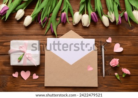 Envelope with blank card, gift box and tulip flowers on wooden background. International Women's Day celebration