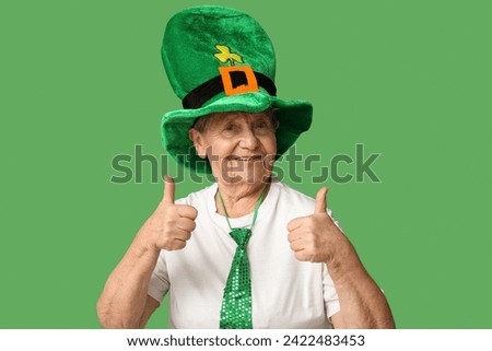 Senior woman in leprechaun hat showing thumb-up gesture on green background. St. Patrick's Day celebration