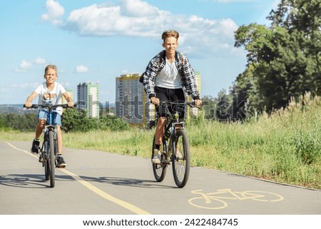 Two young boys are riding their bikes on a bicycle lane in park. They are both wearing casual clothes and look like they are enjoying the warm weather Royalty-Free Stock Photo #2422484745