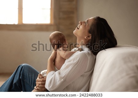 Depressed young mother sitting on floor and holding infant baby on hands, suffering from postnatal depression, motherhood stressful Royalty-Free Stock Photo #2422488033