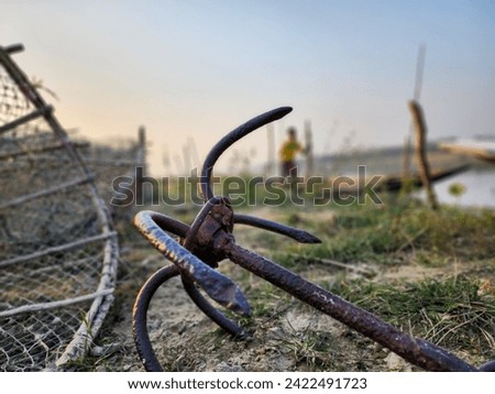 An anchor by the riverside wet land with part of fishing net visible and blurry fishermen in the far background 