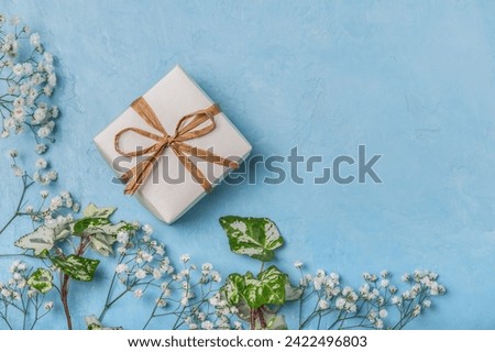 White gift box on a blue background with sprigs of gypsophila. Greeting card for Easter, Happy Birthday, Mother's Day, Father's Day, Wedding Day.