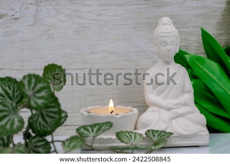 Close up of white marble figurine of Siddhartha Gautama, known as Buddha, with candle burning and decorative flowers, with colorful traditional background