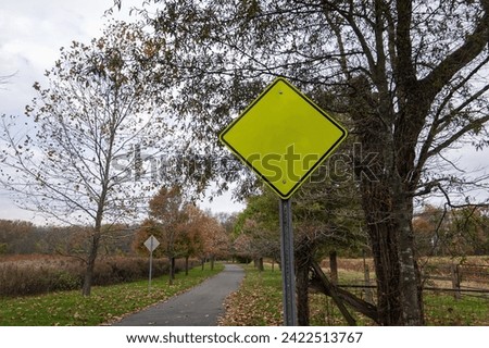 Blank fluorescent green triangular yield sign near a country walking path near trees