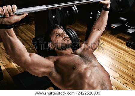 Young muscular man lifting a barbell bench press in the gym. Beautiful body, goal achievement, Sport as a way of life. Royalty-Free Stock Photo #2422520003
