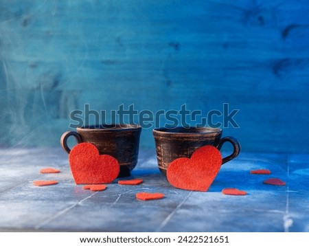 Two cups and red felt hearts on a blue table. A romantic Valentine's day card.