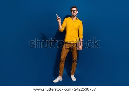 Full length photo of nice young male netbook specs point empty space dressed stylish yellow garment isolated on dark blue color background