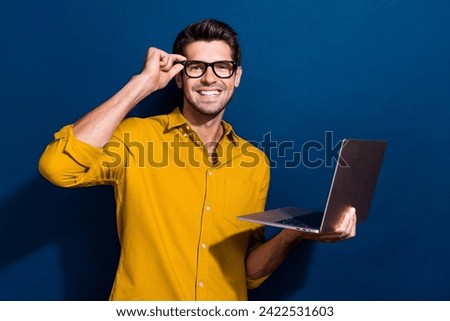 Photo portrait of attractive young man touch specs hold netbook marketer wear trendy yellow clothes isolated on dark blue color background