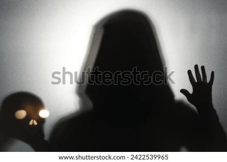 Silhouette of ghost and skull behind glass against light grey background
