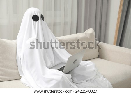 Creepy ghost. Person covered with white sheet using laptop on sofa at home