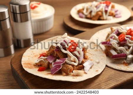 Delicious tacos with vegetables, meat and sauce on wooden table, closeup