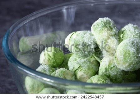 Frozen baby brussels sprouts defrosting in a glass bowl. On a dark stone background