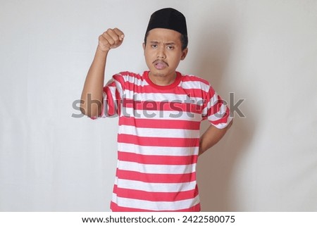 Portrait of unpleasant Asian man in red white stripe t-shirt with skullcap showing disappointed and upset expression. Advertising concept. Isolated image on gray background