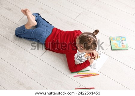 Cute little girl coloring on warm floor indoors. Heating system