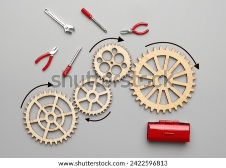 Flatlay picture of wooden gear, handy tool and toolbox on grey background. Mechanism repair.