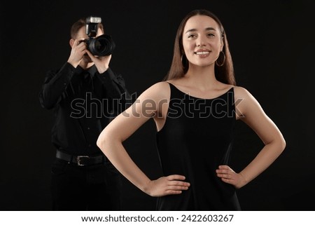 Professional photographer taking picture of beautiful young woman on black background, selective focus