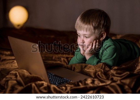 Little boy watching cartoons on a laptop in the bedroom on the bed