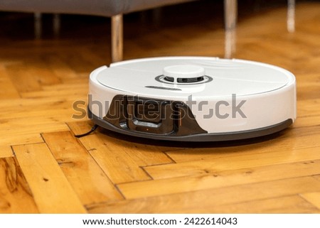 robot vacuum cleaner in modern smart home, robotic vacuum cleaner on wooden or laminate or parquet floor, cleaning dust on tile floors. Modern smart cleaning technology housekeeping. Royalty-Free Stock Photo #2422614043