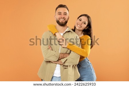 Romantic Love And Relationship. Smiling European Young Couple Hugging Enjoying Time Together, Standing Over Orange Studio Background, Wife Embracing Her Husband From Back Royalty-Free Stock Photo #2422625933