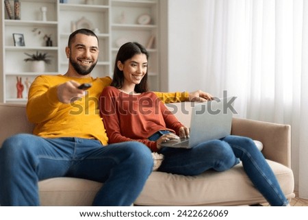 Happy Young Couple Resting On Couch At Home, Man Watching Tv And Woman Using Laptop, Cheerful Millennial Spouses Spending Time Together In Living Room, Enjoying Domestic Leisure, Closeup Royalty-Free Stock Photo #2422626069
