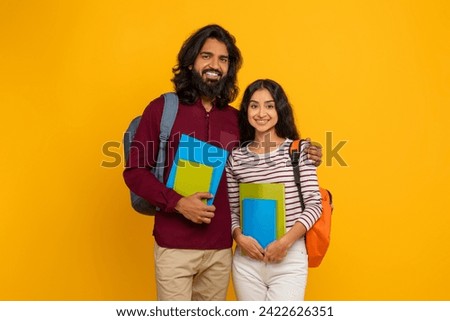 Photo of attractive funny best friends indian man and woman dressed in casual clothing starting college university education isolated yellow color background, embracing and smiling at camera