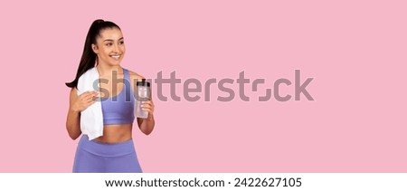Refreshed young woman in purple sports bra and leggings holding water bottle and white towel over her shoulder after gym session on pink background, panorama, free space Royalty-Free Stock Photo #2422627105