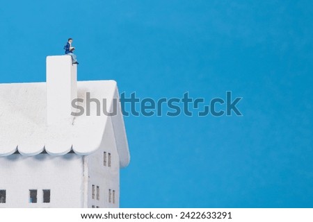 A man reads a book on the chimney of his house, blue background