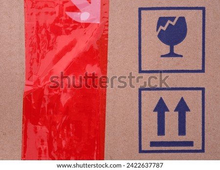 Two signs on cardboard box - Fragile and This Way Up and a red scotch tape on a cardboard