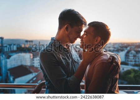 Young happy cute gay couple hugging and kissing on balcony overlooking city  Royalty-Free Stock Photo #2422638087