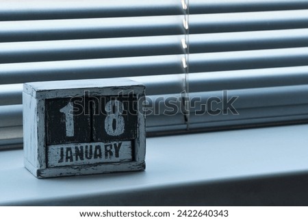Morning January 18 on wooden calendar standing on window with blinds