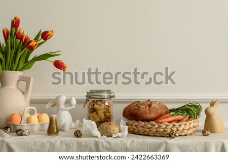 Creative composition of easter living room interior with bread, basket, carrot, vase with spring tulips, easter bunny sculpture, colorful easter eggs and personal accessories. Home decor. Template.