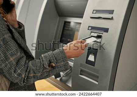 Close-up of a young woman's hand as she smoothly inserts her debit card into the ATM, accessing her financial resources with ease. Royalty-Free Stock Photo #2422664407