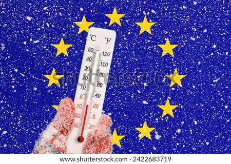 Flag of Europe Union and snowfall. Celsius and fahrenheit scale thermometer in hand. Ambient temperature minus 5 degrees.