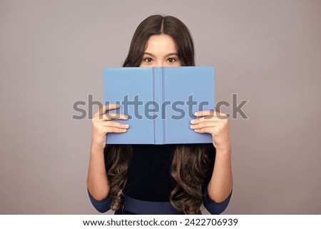 Schoolchild, teenage student girl hold book near eyes on gray isolated studio background. School and education concept. Back to school. Face hidden with book.