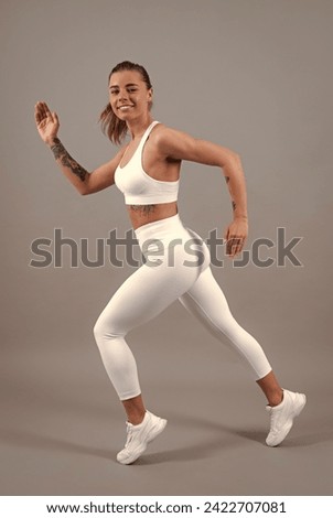 Workout sport motivation concept. Young fitness woman runner stretching legs before run. Sporty woman runner on gray background. Dynamic movement. Sport and healthy lifestyle.