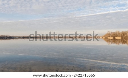 Reflection in the water of river of a cloudy sky and trees far on the horizon. Clear day, slight haze. Delicate tones. Horizontally Royalty-Free Stock Photo #2422715565