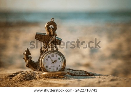 Maritime Moments: Pocket Watch and Anchor - A pocket watch rests on a sandy shore, draped over an anchor.