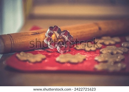 Close up - four-leaf clover-shaped, floured cookie cutter and raw cookies patterned with it on a red background, with a rolling pin