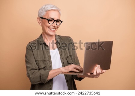 Photo of smiling amazon seller specialist in ecommerce mature business woman looking laptop her stats isolated on beige color background