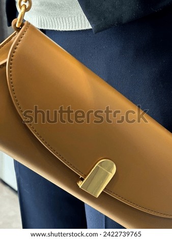 Closeup picture of look collecting details at the department store. Camel color leather bag with golden furnitures. At the background of navy trousers