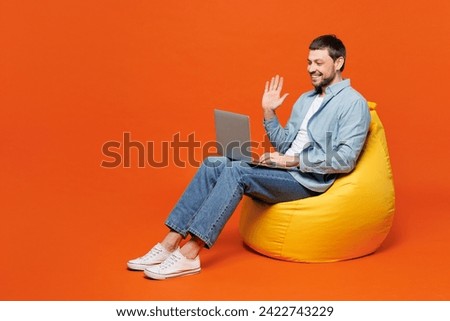 Full body happy young IT man he wears blue shirt white t-shirt casual clothes hold use work on laptop pc computer waving hand isolated on plain red orange background studio portrait. Lifestyle concept
