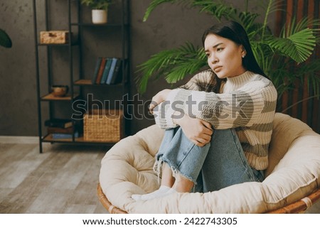 Full body young tired sad thoughtful depressed woman wears casual clothes sits on armchair stay at home hotel flat rest relax spend free spare time in grey living room indoor. People lounge concept Royalty-Free Stock Photo #2422743305