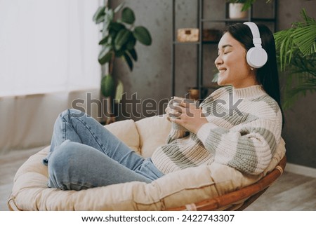 Full body young woman wears casual clothes listen to music in headphones drink tea sits on armchair stay at home hotel flat rest relax spend free spare time in grey living room indoor. Lounge concept Royalty-Free Stock Photo #2422743307